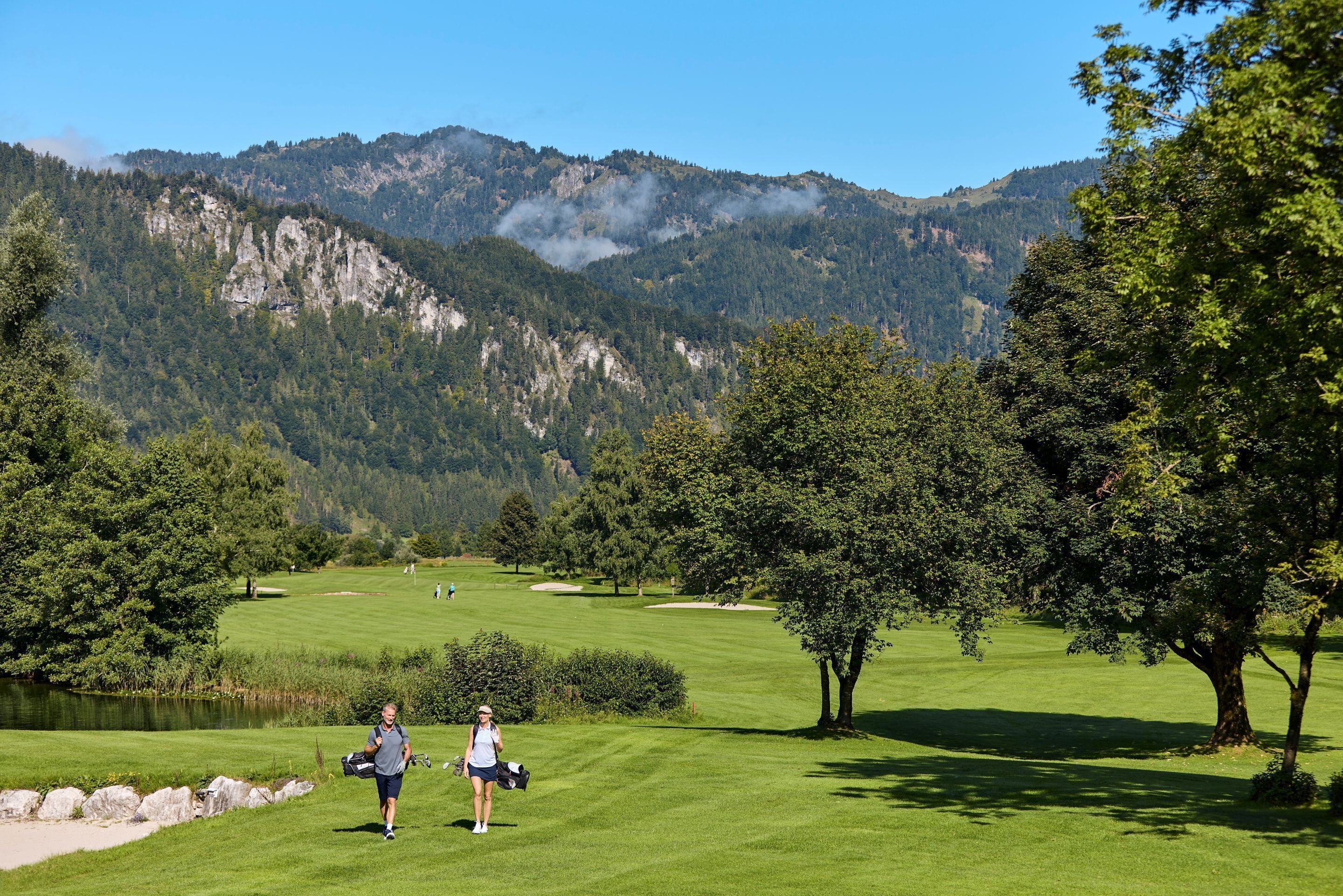 A golf course with a lake, trees, and mountains in the background.