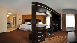 A hotel room with a large bed, a desk, a chair, a TV, and a window with curtains.
