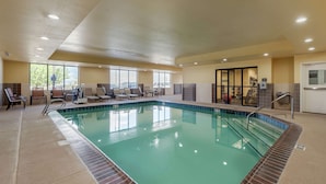 An indoor swimming pool with clear water, surrounded by lounge chairs and a sunbed area.