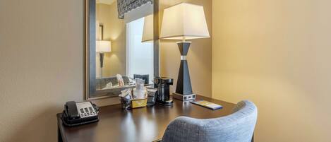 A hotel room desk with a telephone, a lamp, a coffee maker, and a basket of toiletries.