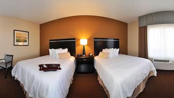 A hotel room with two beds, a nightstand with a lamp, a chair, and a large window with curtains.