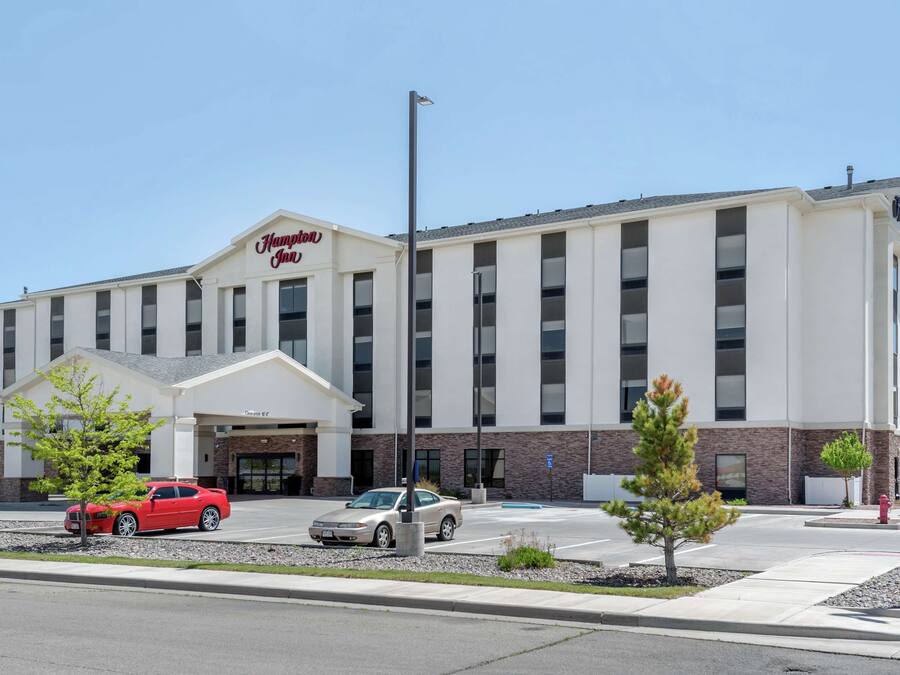 Un hotel Hampton Inn con una facciata moderna, un parcheggio e alcune auto parcheggiate davanti.