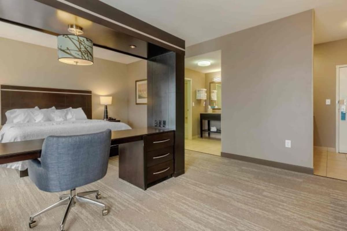 A hotel room with a bed, desk, chair, and a large mirror.
