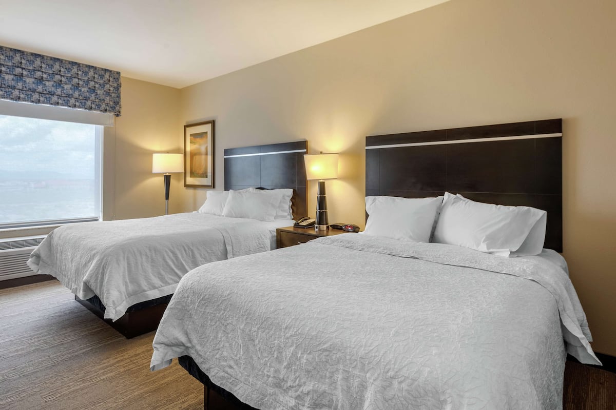 A hotel room with two beds, a large window, and a view of the city.