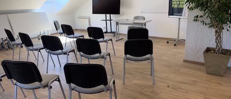 A conference room with a large screen, a whiteboard, and several chairs arranged around a table.