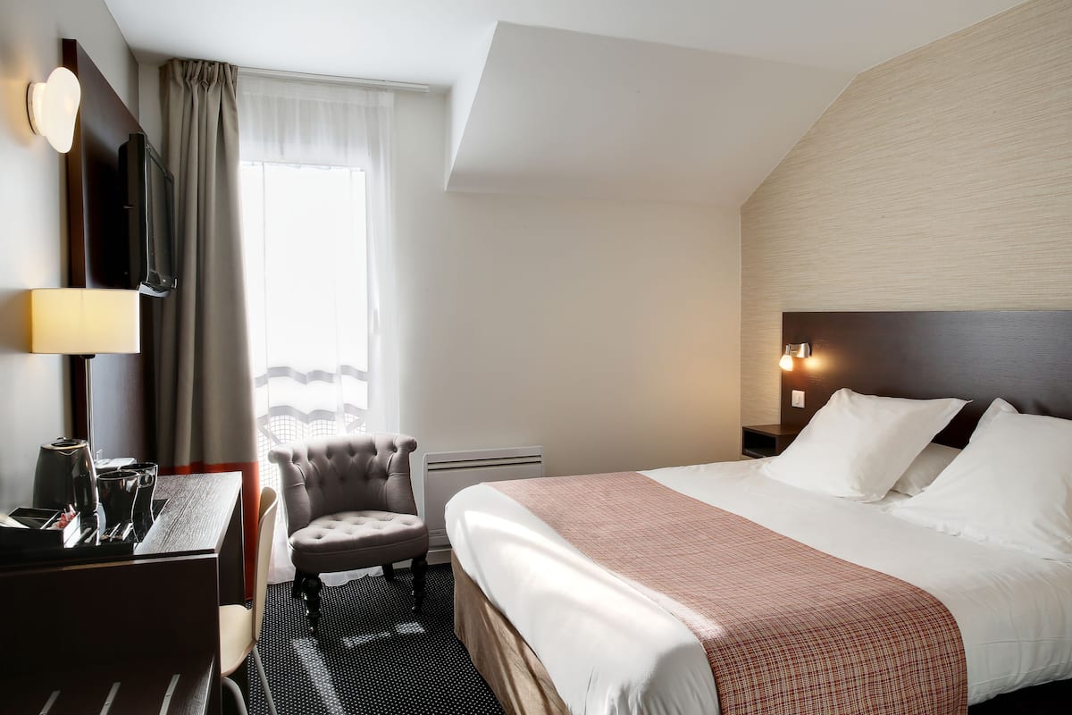 A hotel room with a bed, a desk, a chair, a TV, and a window with curtains.