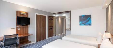 A hotel room with a bed, a desk with a chair, a television, a wardrobe, and a bathroom.