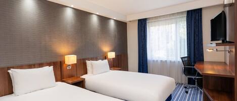 Habitación de hotel con dos camas, un escritorio, un televisor y una ventana con cortinas.