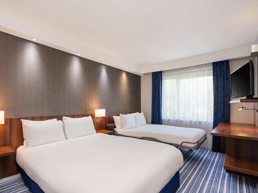 A hotel room with two beds, a TV, and a large window with curtains.