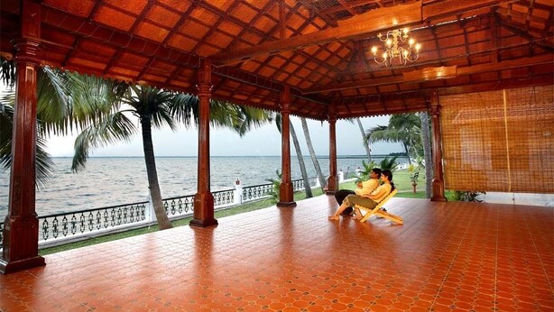 A covered outdoor area with a tiled floor, wooden pillars, and a view of the sea. - Coco Bay Resort (Kottayam)