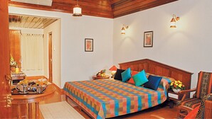 A bedroom with a wooden headboard, a colorful bedspread, and a nightstand with a lamp and flowers. - Coco Bay Resort (Kottayam)