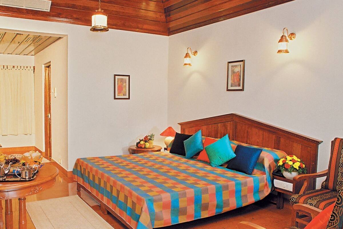 Un dormitorio con cabecera de madera, una cama con ropa de cama colorida, una mesita de noche con una lámpara y una silla.