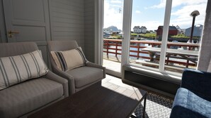 Une pièce avec deux canapés gris, une table basse en bois et une grande fenêtre donnant sur un quai et des bâtiments.