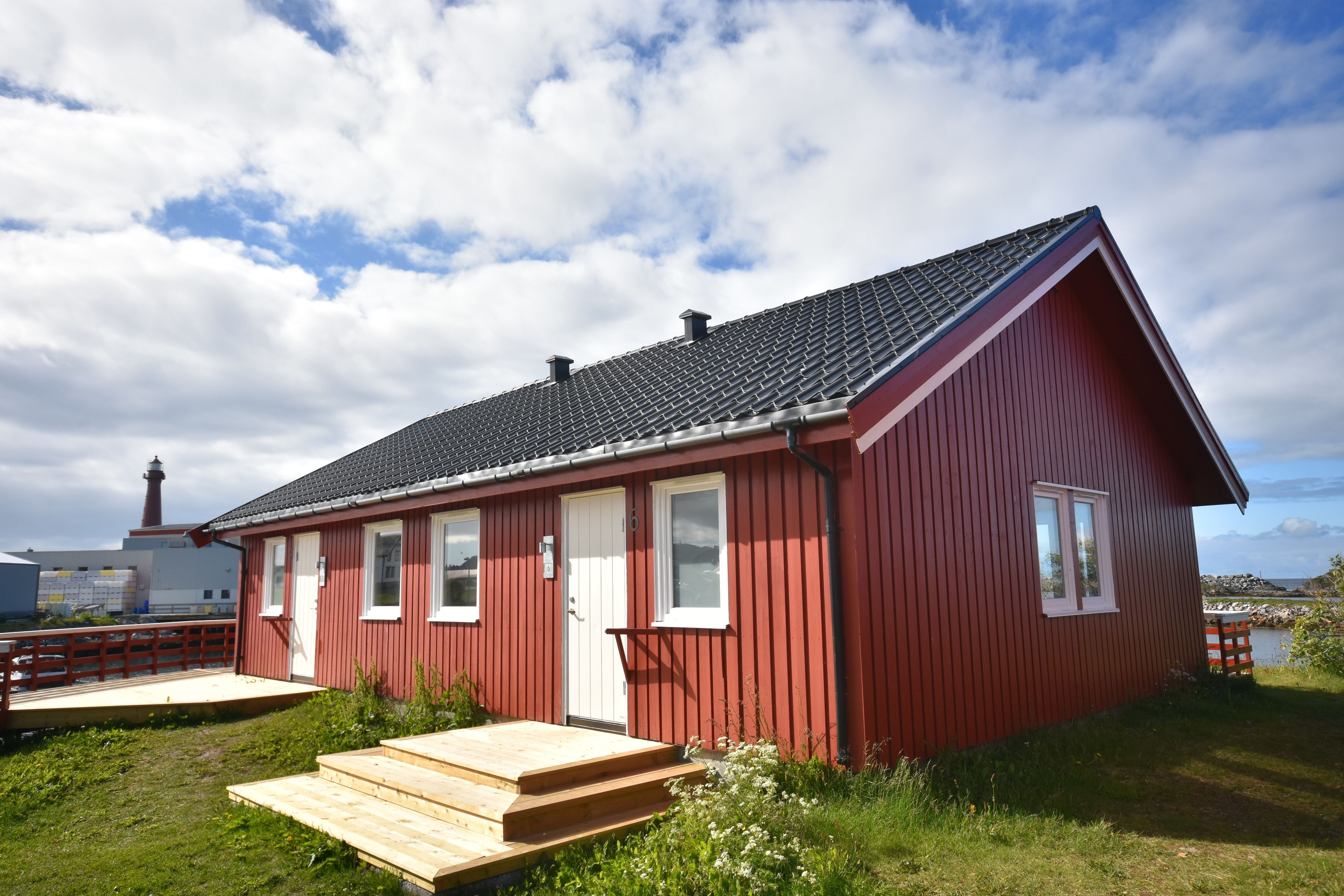 Una casa de madera roja con techo inclinado, un porche delantero y una pequeña terraza.