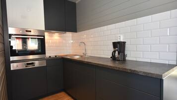 A modern kitchen with dark cabinetry, a stainless steel oven, a sink, and a coffee maker.
