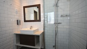 A modern bathroom with white subway tiles, a white sink, a dark-toned vanity, a glass shower enclosure, and a mirror with a wooden frame.