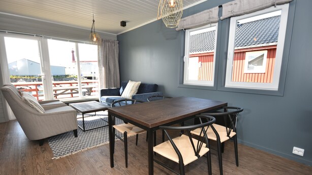 A modern living room with a wooden floor, a sofa, a dining table with chairs, and large windows with curtains.