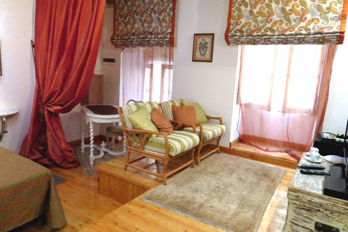 Una habitación acogedora con suelo de madera, un sofá a rayas, una mesita y una ventana con cortinas.