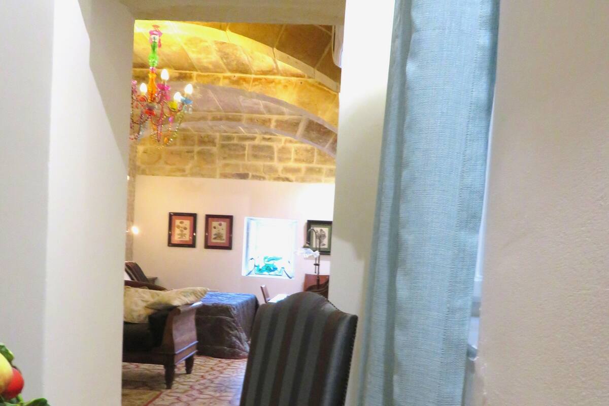 Un comedor con una mesa de madera, una silla y vistas a una sala de estar con un sofá y un tapiz estampado.