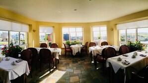 A dining area with tables set for four, large windows with views of the outside, and a stone floor. - Lehinch Lodge (Lahinch)
