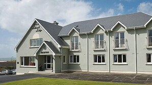 A large, two-story building with a prominent entrance, multiple windows with balconies, and a well-maintained lawn in front. - Lehinch Lodge (Lahinch)