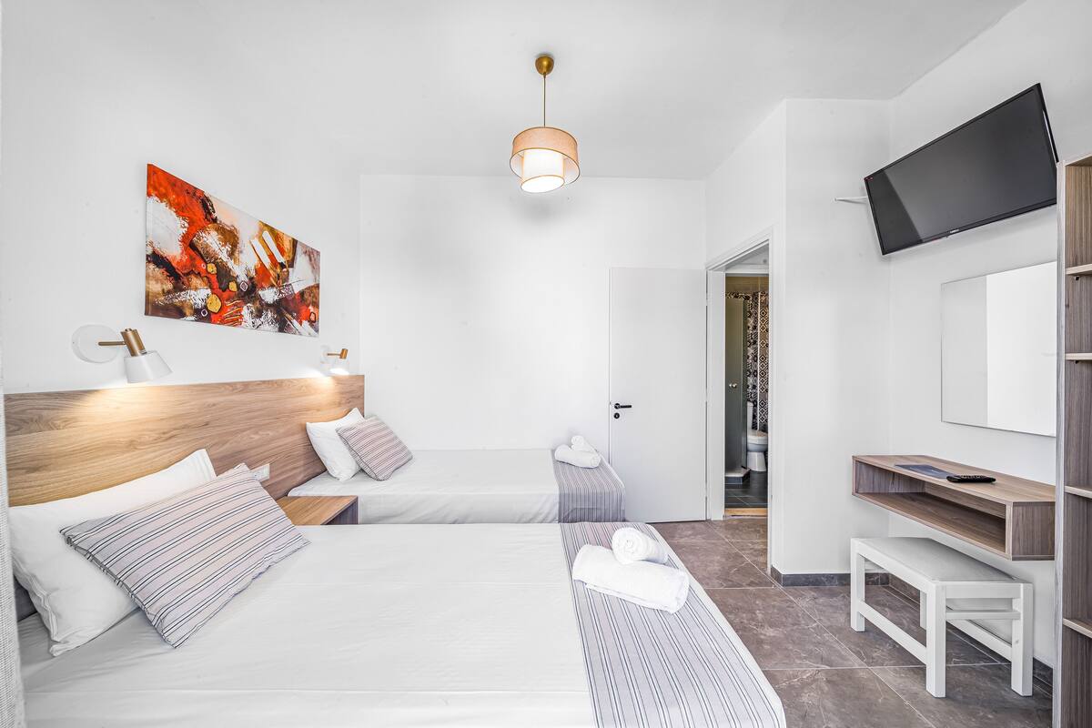 A modern hotel room with two beds, a TV, a painting, and a wooden desk.