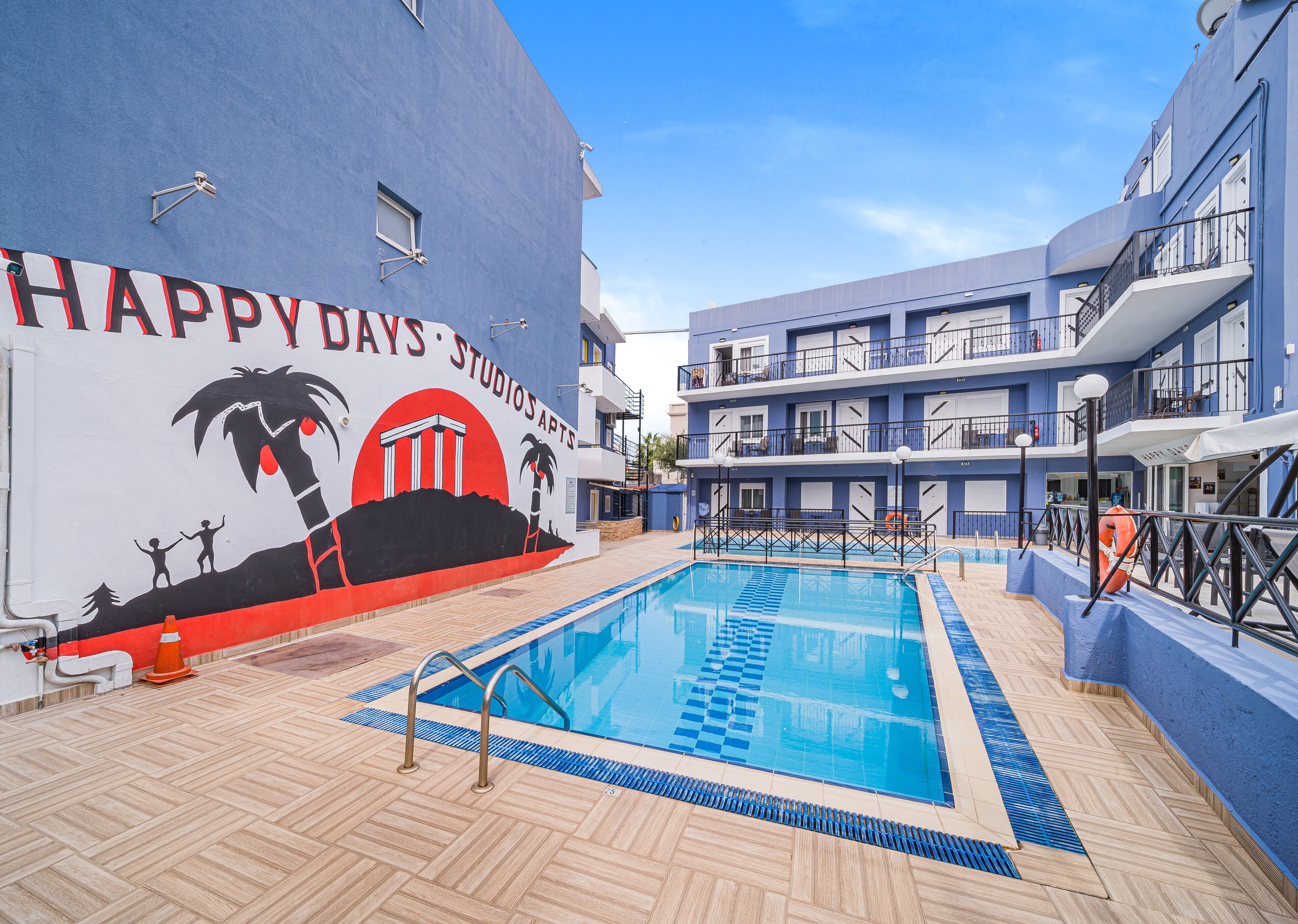 Zona de piscina con un mural, piscina con escalones y un edificio con balcones.