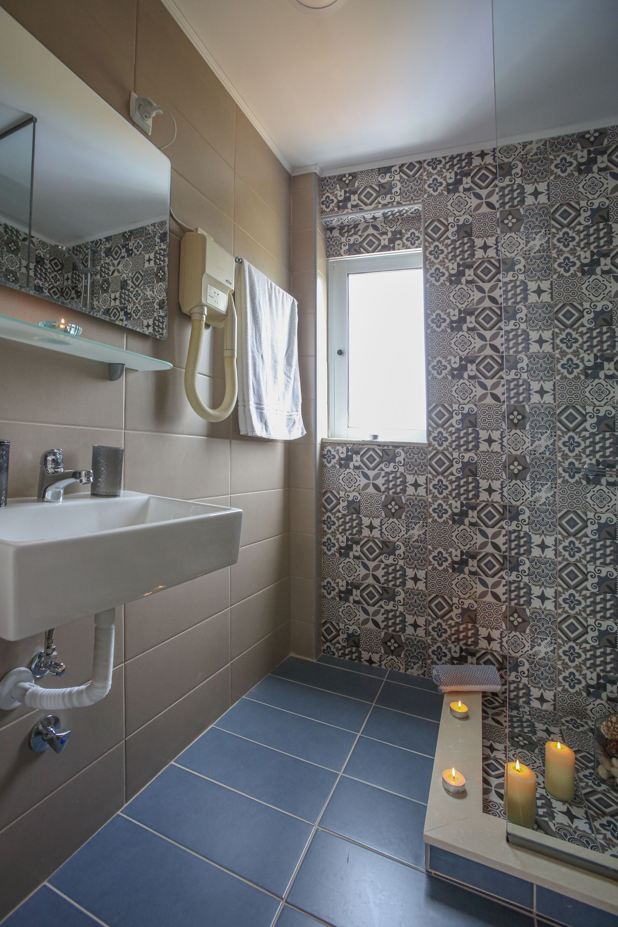 A bathroom with a sink, mirror, towel rack, and patterned tiles.