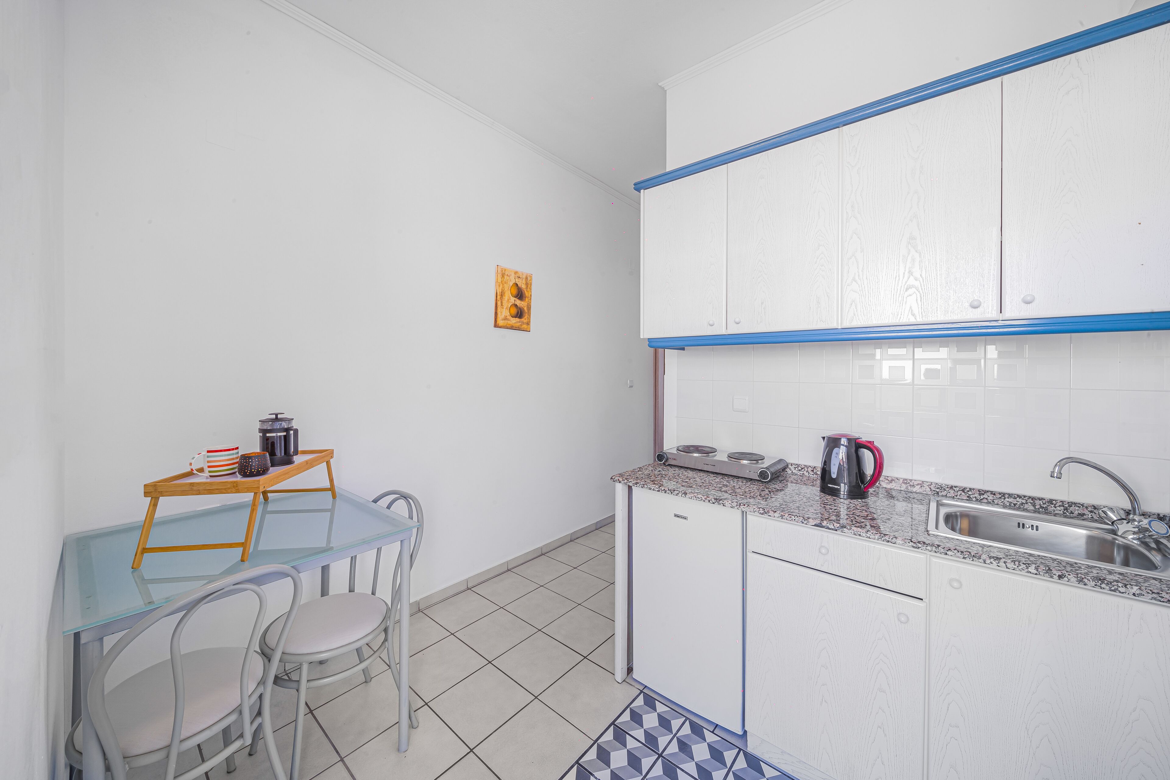 A compact kitchen with white cabinets, a granite countertop, a sink, and a small dining area with a glass table and two chairs.