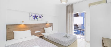 A hotel room with two beds, a wooden headboard, a ceiling light, a window with curtains, and a view of the outside.