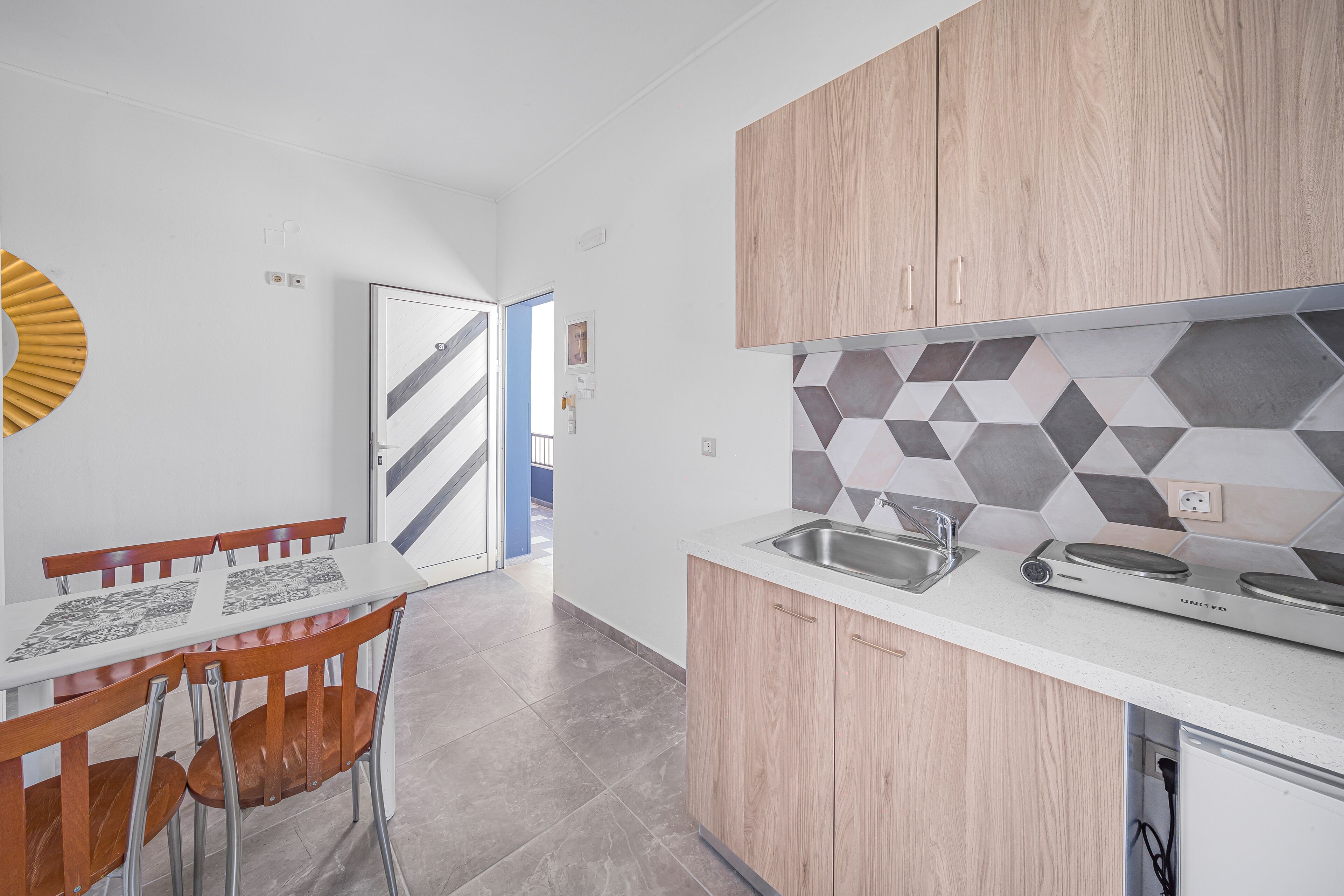 Una cucina moderna con piano di lavoro bianco, mobili in legno e zoccolo a parete in piastrelle geometriche.