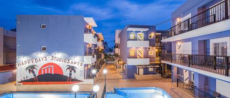 Un hotel con piscina, varios balcones y un cartel que dice HappyDays Studios Apartments.