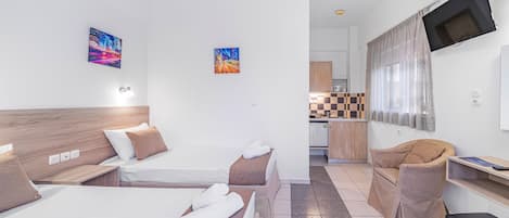 A hotel room with two beds, a sofa, a TV, and a kitchenette.