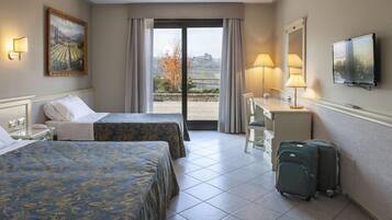 Ein Hotelzimmer mit zwei Betten, einem Schreibtisch, einem Sessel, einem Fernseher und Blick ins Freie.