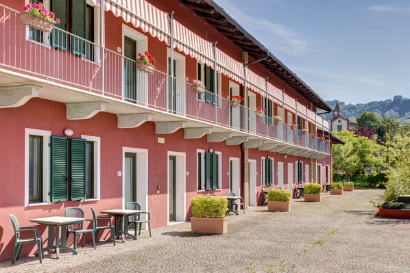 A red building with balconies, outdoor seating, and potted plants. - Hotel SantaMaria Langhe (La Morra)
