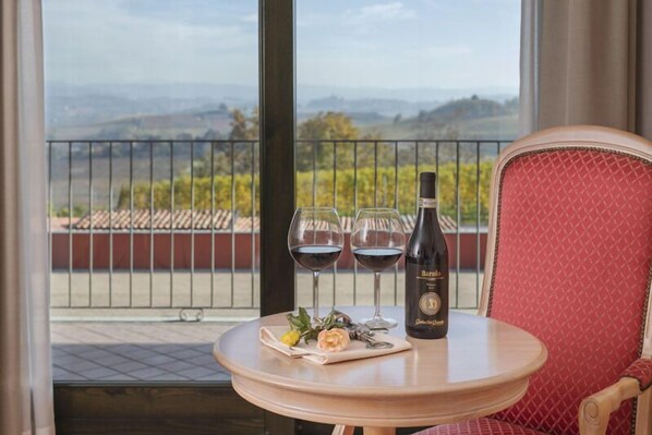 A table with a bottle of wine, two glasses, and a small bouquet on a balcony overlooking a vineyard. - Hotel SantaMaria Langhe (La Morra)