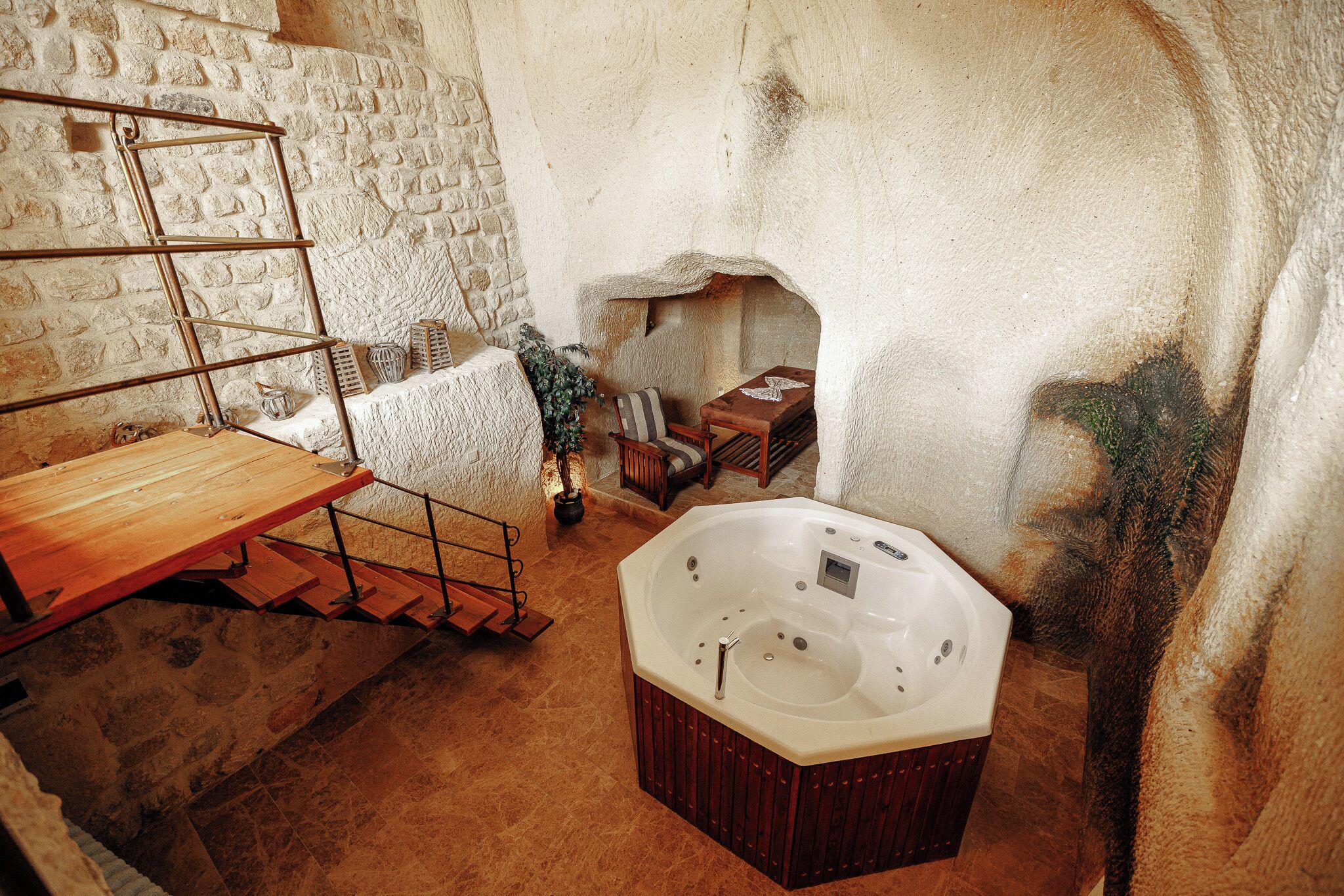 Une pièce aux murs de pierre, avec un banc en bois, un jacuzzi et un escalier.