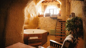 A rustic stone bathroom with a wooden bathtub, a bench, and a plant. - Yunak Evleri Cappadocia (Ürgüp)