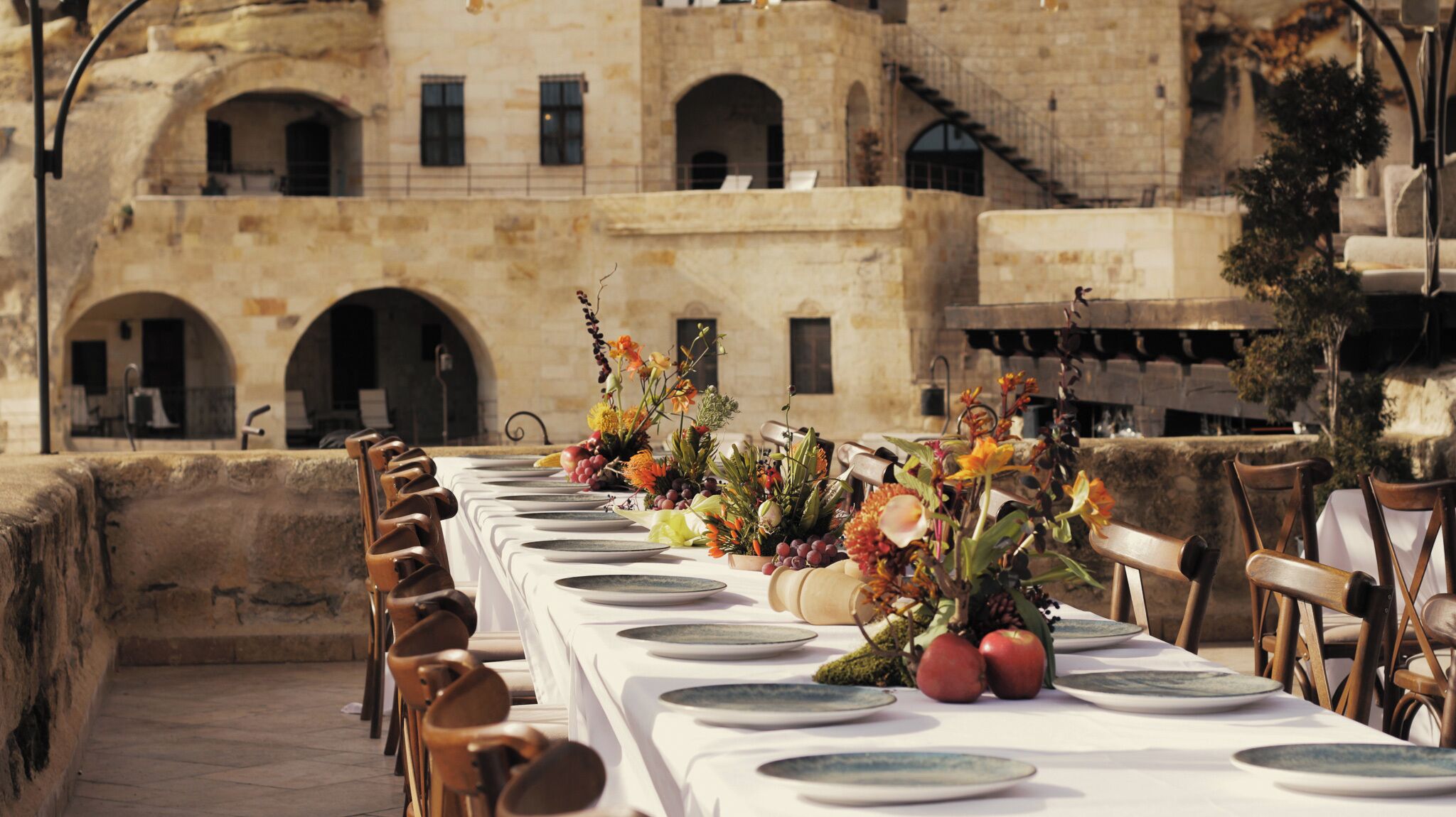 A long dining table set with white tablecloths and plates, surrounded by wooden chairs.