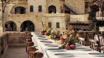 A long dining table set with white tablecloths and plates, surrounded by wooden chairs.