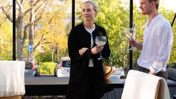 A person holding a wine glass with a straw, standing by a window with a view of trees and parked cars.