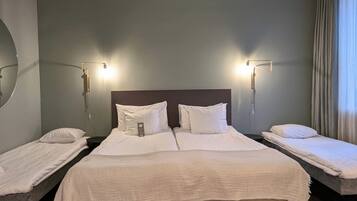 Una habitación de hotel con dos camas individuales, una cama grande y una mesita de noche con lámpara.