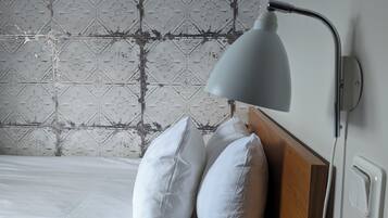 A neatly made bed with white linens and two pillows, a modern wall-mounted lamp, and a patterned tile backsplash.