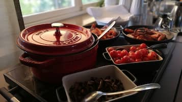 Ein reichhaltiges Buffet mit verschiedenen Speisen, darunter ein roter Topf, Schalen mit Kirschtomaten und eine Schale mit Pilzen.