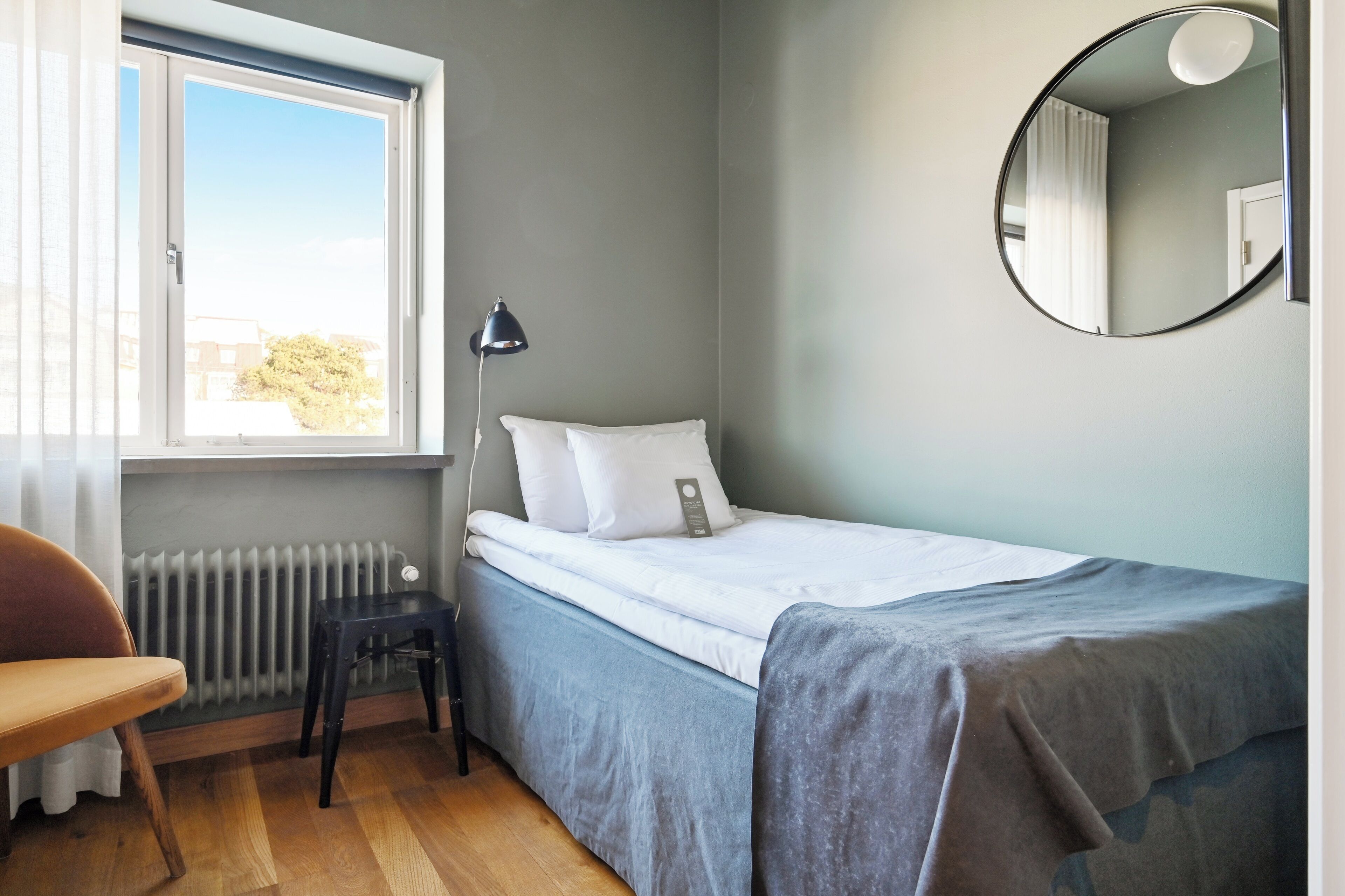 A bedroom with a bed, a chair, a radiator, a window, and a mirror.