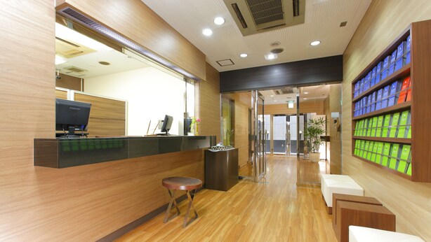 A reception area with a wooden floor, a reception desk, a computer, and a seating area with a plant. - Flexstay Inn Sugamo (Tokyo)