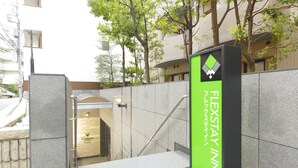 A hotel entrance with a modern design, featuring a prominent green signboard and a staircase leading to the entrance. - Flexstay Inn Sugamo (Tokyo)