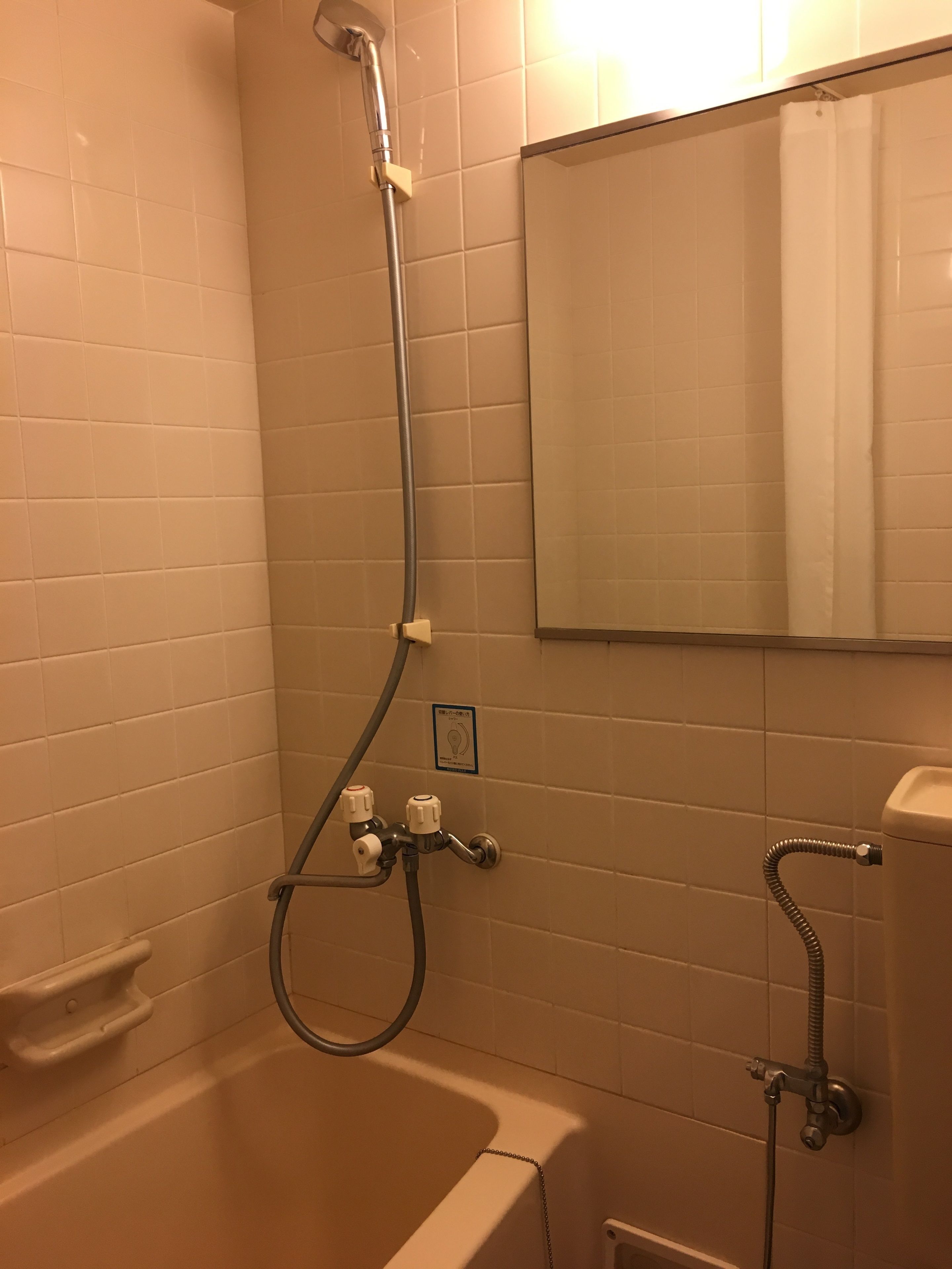 A bathroom with white tiled walls, a bathtub, a shower with a handheld showerhead, and a wall-mounted sink.