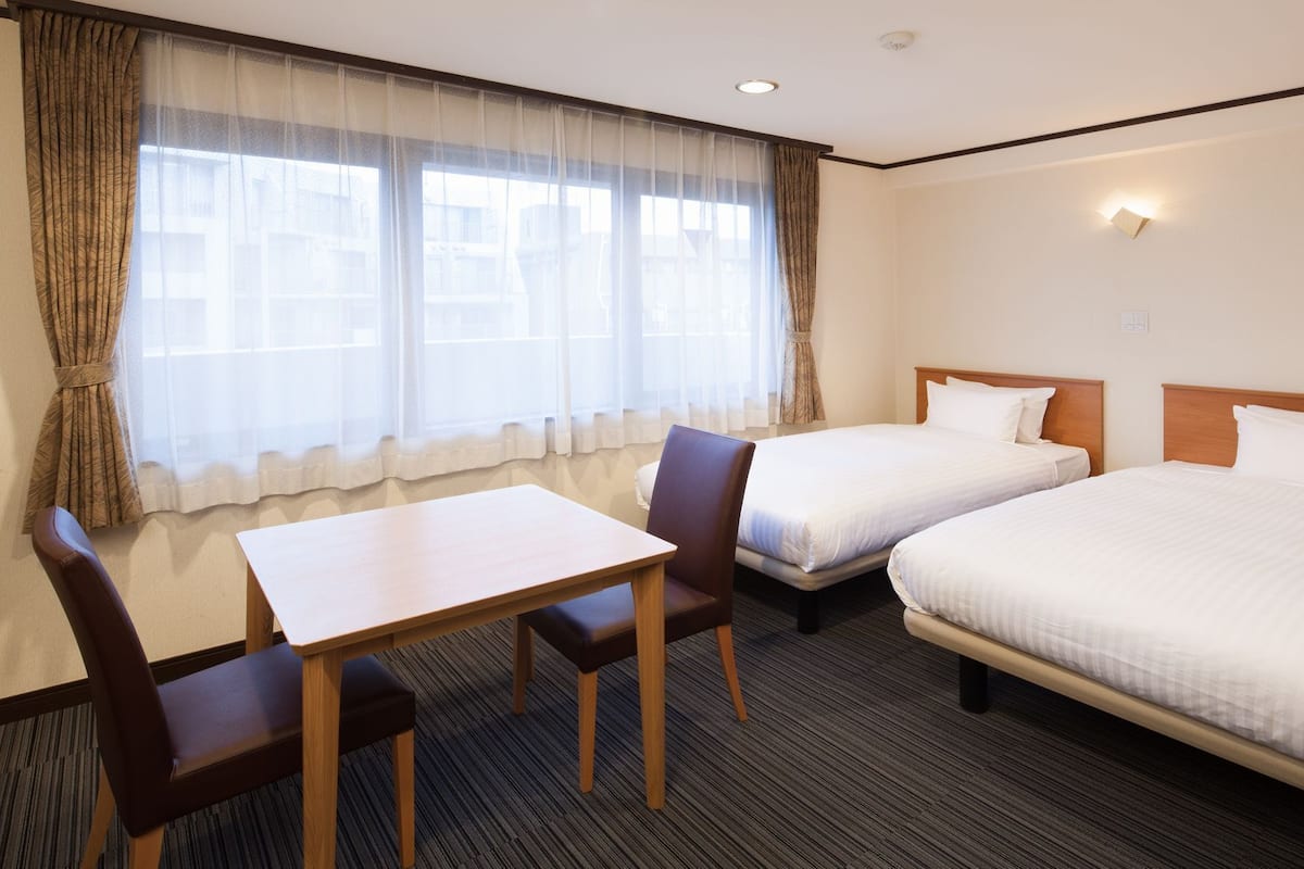 Quarto de hotel com duas camas, uma mesa e uma cadeira.