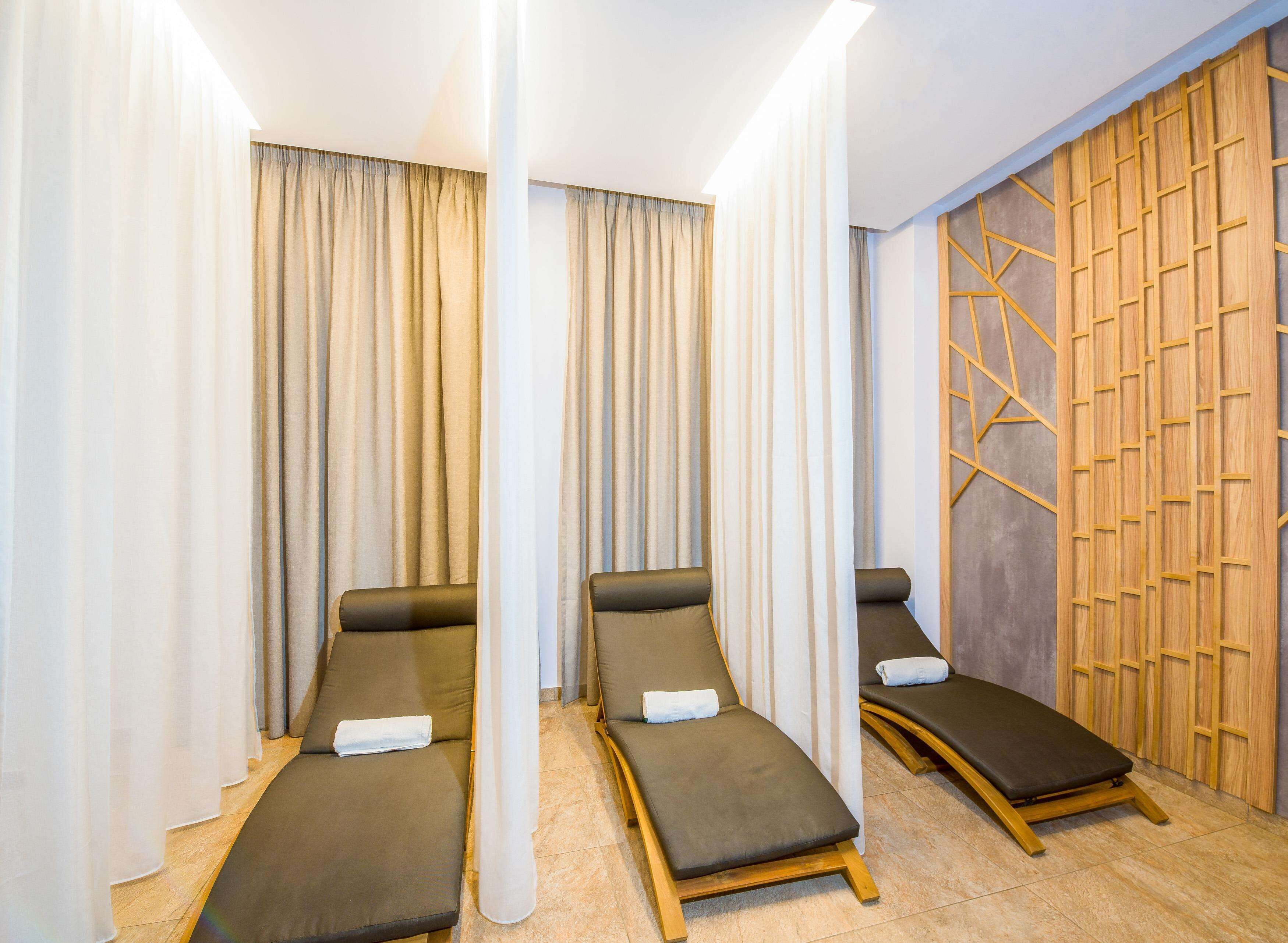 A spa room with three massage tables, beige curtains, and a wooden wall panel.